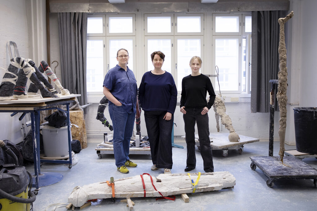 Kolme naista seisoo huoneessa ikkunan edessä. Ympärillä on keskeneräisiä taideteoksia.